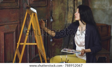 Young woman artist draw pictrure with watercolor paints and brush on easel canvas