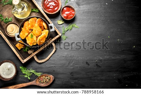 Nuggets from chicken meat with sauces on a tray. On the black chalkboard.