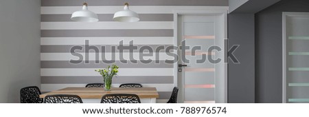 Modern dining room with wooden table, openwork chairs and white and grey striped wall, panoramic view