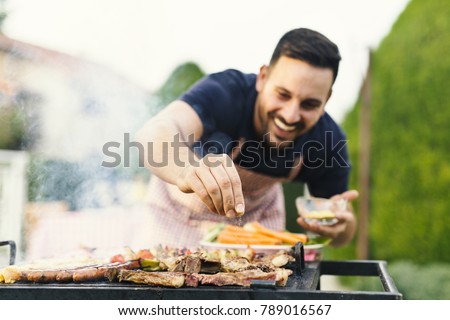 Smiling man seasoning meat on the grill Royalty-Free Stock Photo #789016567