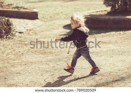 Baby boy in blue jacket and jeans walk with stick on sunny day on natural background. Energy, activity, leisure concept. Child, childhood, lifestyle.