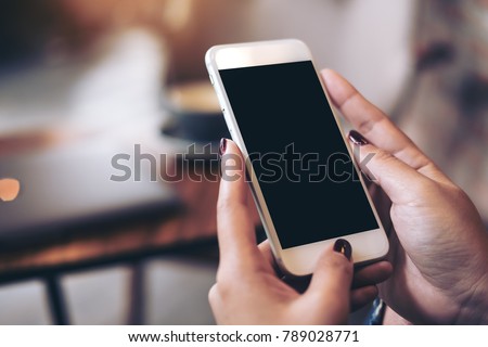 Mockup image of woman's hands holding mobile phone with blank black desktop screen in cafe