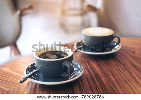 Closeup image of two blue cups of hot latte coffee and Americano coffee on vintage wooden table in cafe Royalty-Free Stock Photo #789028786