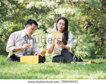 Asian business man and woman sitting and working in the park. Business talk and relaxing outside office.