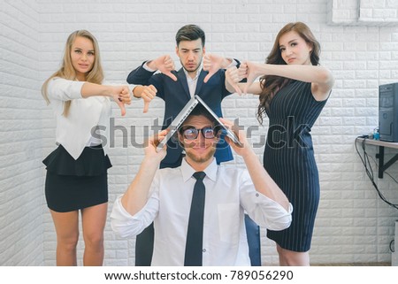 Colleagues business team pointing thumbs down bad negative gesture to business man while project failed in the office, businessman put the laptop on the head, business concept