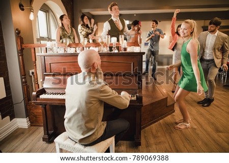 Wedding guests are enjoying a dance while the father of the bride plays piano music. 