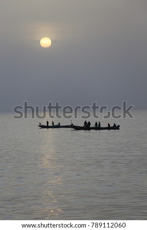 View of small wooden boats with fishermen on board. Picture taken early in the morning near Goree island in Senegal. Silhouettes of the boats can be seen on the calm sea under the sun rising. 