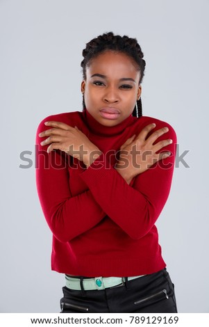 African-American gir stands embracing herself with hands demonstrating the cold. On a gray background.