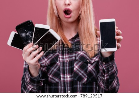 A girl holds several smartphones with broken screens, opening her mouth in surprise. Pink background. Close-up.