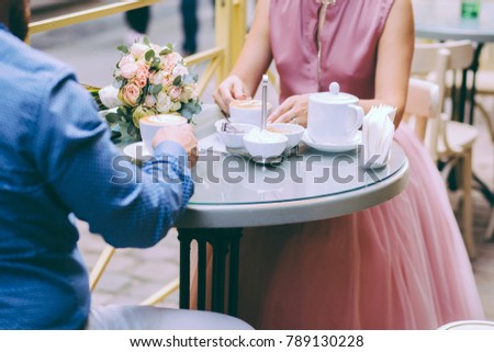 Romantic close up picture of couple with two cups with cuppuccino. Unrecognizable bride and groom drinking coffee while sitting outdoor in round table.