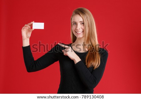 A girl holding an empty business card and showing a finger at it. On a red background.