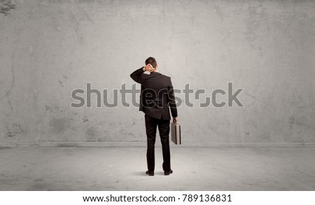 A confused sales person having a dilemma, standing with his back in empty grey urban environment concept