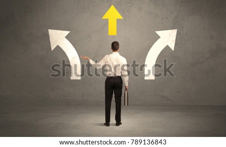 A confused businessman facing a grey urban wall with a yellow arrow pointing in the right direction concept