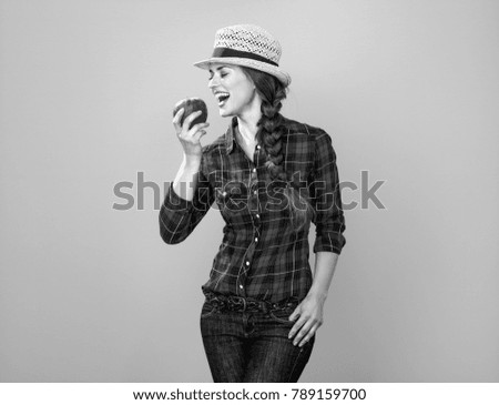 Healthy food to your table. Portrait of smiling young woman grower in checkered shirt on yellow background eating an apple