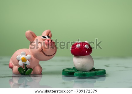 Figurine of a small piggy with a white flower and a mushroom, green background