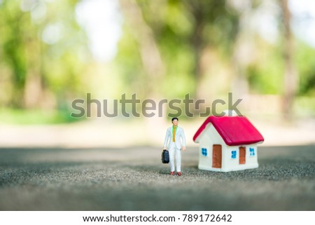 Miniature people, businessman standing with mini house on green nature background using as business, financial and property concept