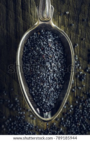Poppy seeds in a spoon on a wooden background. Macro shot. Top view.