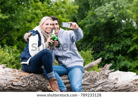 Woman and man drinking beer taking selfie while hiking in forest