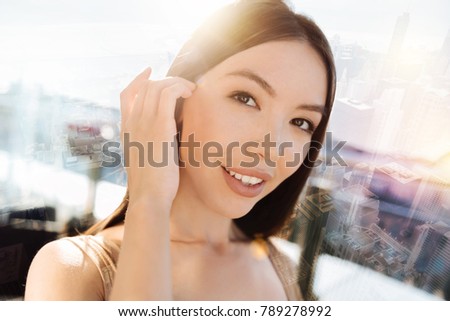 Young model. Pretty female person keeping smile on her face and touching hear while looking forward