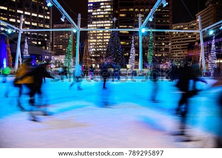 Ghostly figures of ice skaters at the Galavan Center in Salt Lake City, UT. create a holiday scene with city lights and Christmas lights in the background.