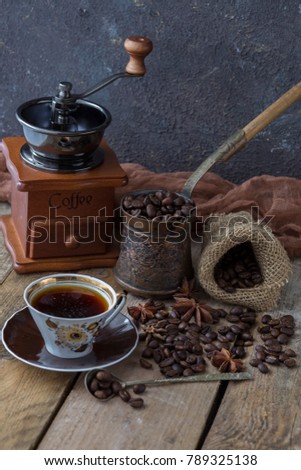 on a wooden table a coffee grinder, a Turk, a cup of coffee, a grains of coffee