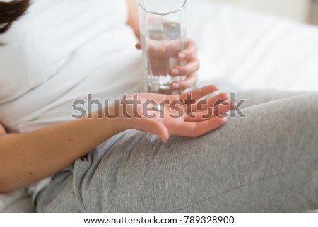 Stressed woman drinking pill or medicine with glass of water on bed at home after wake up in the morning Royalty-Free Stock Photo #789328900