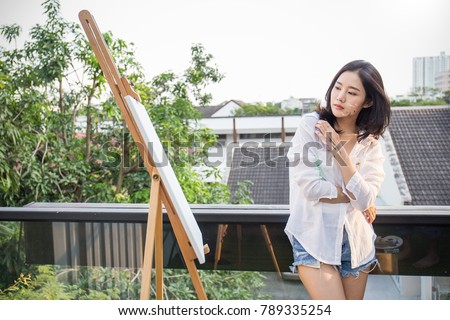 Portrait of asian beautiful woman paint in her art studio outdoor. Young asian girl holding her paintbrush. Artist workshop education concept
