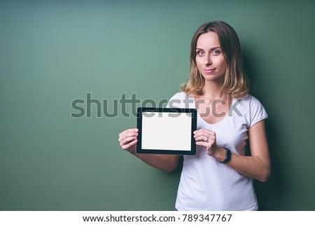 Digital technology. Young pretty woman holding tablet computer with copy space on the screen against green wall.