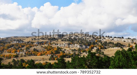 Landscape with multicolor trees (red, green, yellow, orange, brown) in Ay-Petri mountain  (plateau) and cloud sky in sunny autumn day. Crimea, near far from Yalta
