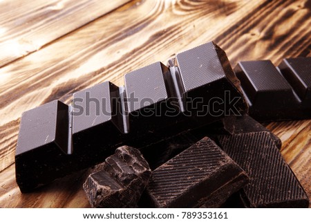 Dark brown chocolate pieces, stacks culinary wooden background.