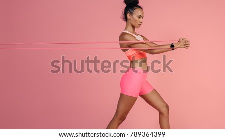 Sportswoman exercising with resistance band. Female with working out with elastic band on pink background.