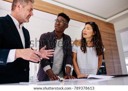 Interracial couple having consultation with a real estate agent inside a new home. Mature male realtor discussing the contract with customer. Royalty-Free Stock Photo #789378613