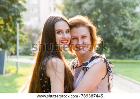 Closeup Portrait of Adult Daughter and Mother Outdoors. Pretty Brunette and Her Mom are Looking at the Camera in the Park in Summer.