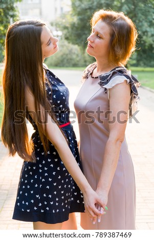Closeup Portrait of Adult Daughter and Mother Outdoors. Pretty Brunette and Her Mom are Looking at the Camera in the Park in Summer.