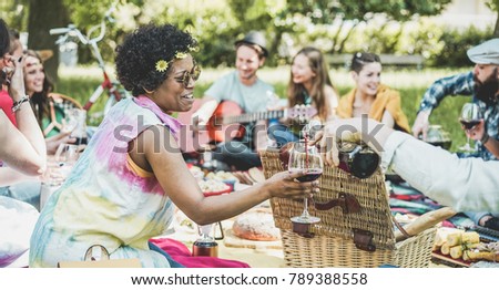 Group of friends making picnic lunch and drinking wine outdoor - Young people having fun while eating and relaxing - Focus on african girl face - Youth lifestyle, holidays and friendship concept 