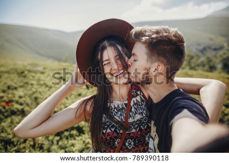 wanderlust and travel together concept. stylish couple travelers in hat making selfie at mountains. hipster family smiling and kissing on top of mountain. space for text. atmospheric moment