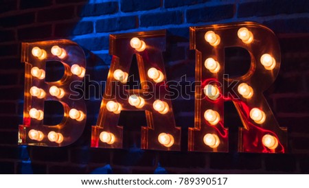 Signboard with the word BAR on the background of a blue brick wall. The letters are decorated with incandescent lamps.