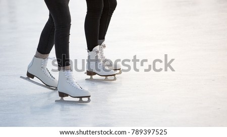 close-up of women's legs on skates in winter on an open skating rink, place for text/ The ice skates of two friends skating together on a winter afternoon/ Winter time, outdoor activities  - concept
