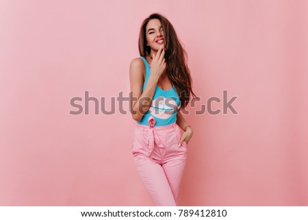 Refined caucasian girl with long hairstyle standing on pink background with smile. Slim blissful brunette woman relaxing in studio.