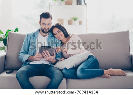 Pleased cheerful relaxed beautiful cute couple of lovers is buying ordering products on the internet and choosing furniture for their house using digital tablet cozy comfortable atmosphere
