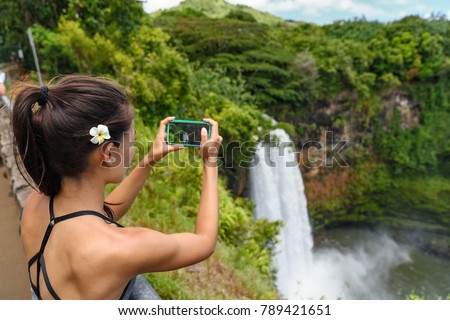 Hawaii travel tourism. Tourist woman taking pictures with mobile phone photo app of Wailua Falls waterfall on Kauai, Hawaii, USA.