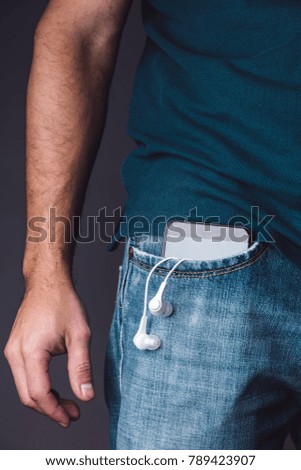 Smartphone with earphones on a caucasian young adult male jeans pocket.
