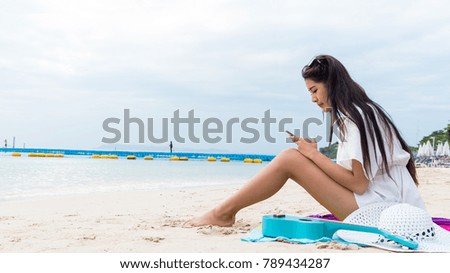An Asian girl in a white dress sitting on a beachfront smartphone for a vacation.lying on the beach.