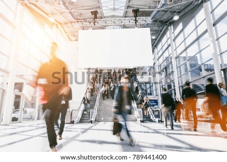 large crowd of anonymous blurred people at a trade show, including banner for text