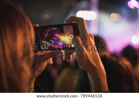 woman using mobile phone taking photo of live show concert with blurry stage as background. have a copy space for text.