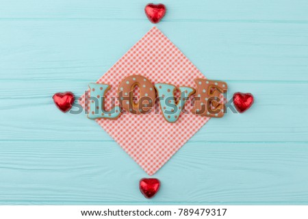 Blue and brown letters love from cookies. Heart shaped sweets wrapped in a bright red foil lying on a wooden background, top view. Happy Valentines Day background.