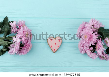 Heart shaped cookie and chrysanthemums. Gentle composition for Valentines Day, blue wooden background. Pink heart on light blue wooden table. Love and romance.