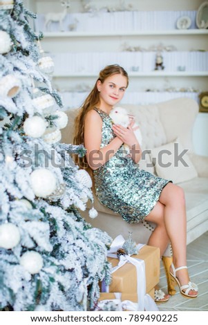 Little beautiful girl hugs a white rabbit, on background of Christmas tree and cozy light room