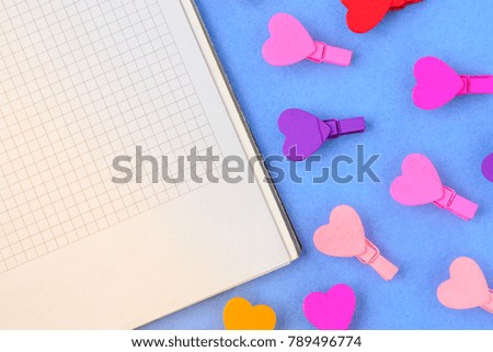 White paper and small wooden colored hearts on a blue background. Concept notes for Valentine's Day