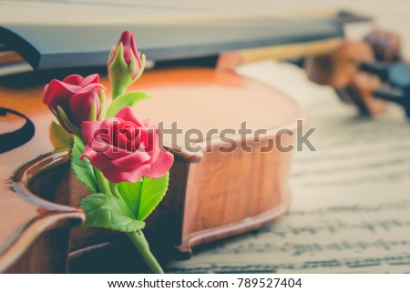 Valentine's day / eternal love or special occasion concept : Artificial three red roses put near a stradivarius type violin on blurred musical notes in a romantic love song sheet music. Vintage style.